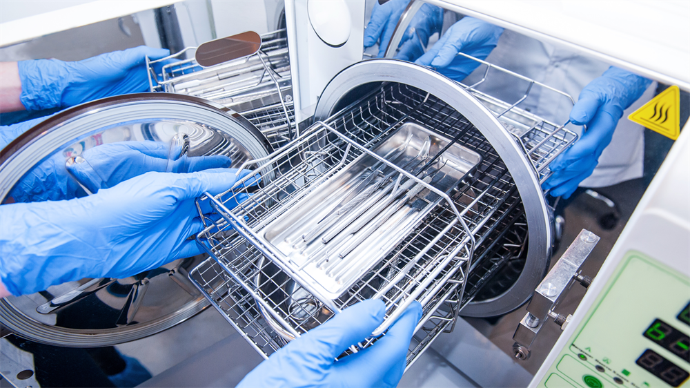 A technition inserts dental instruments into an autoclave for steam sterilization.