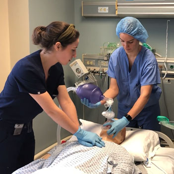 Nurses work with a training dummy in a hospital room.