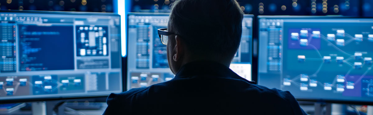 A man faces multiple monitors as he maintains cybersecurity.
