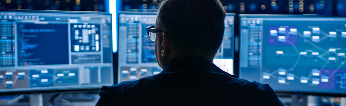 Cybersecurity-Roundtable-banner A man faces multiple monitors as he maintains cybersecurity.