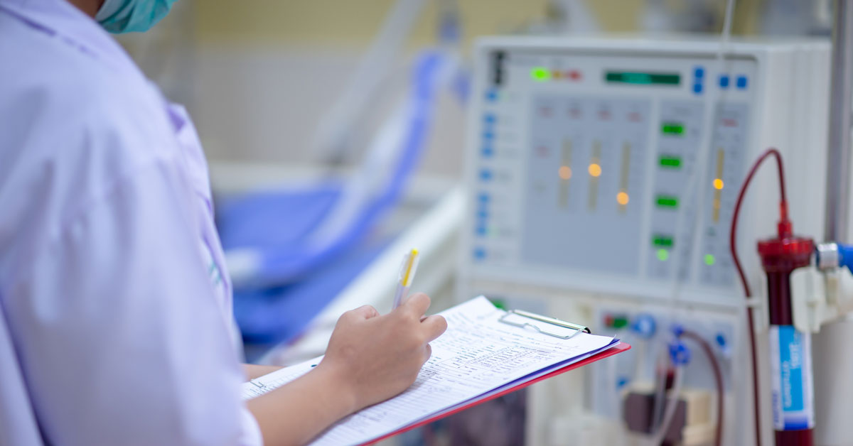 A nurse holding a clipboard checks a dialysis machine