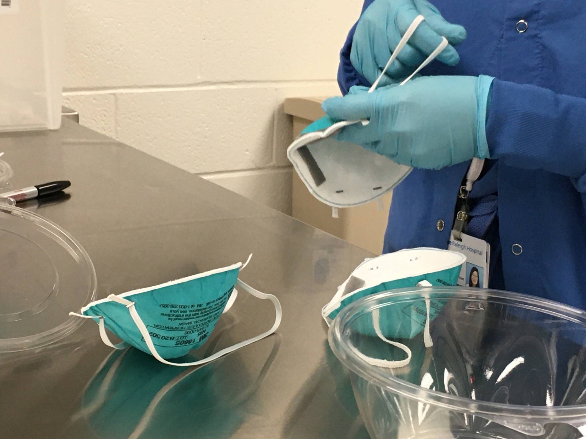 Glove hands pull at the bands of N95 masks, checking the elastic before they are reused.