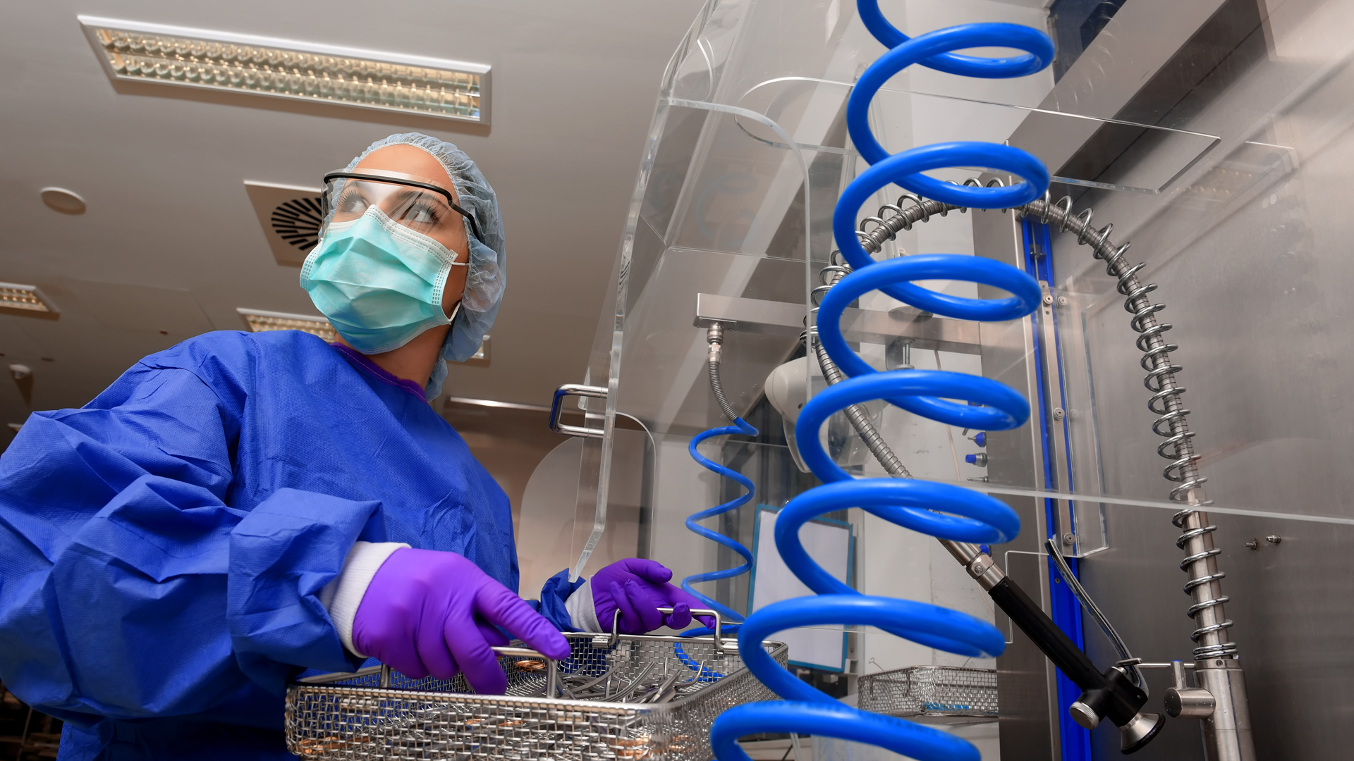 A hospital sterilization professional in full PPE prepares medical instruments for cleaning.