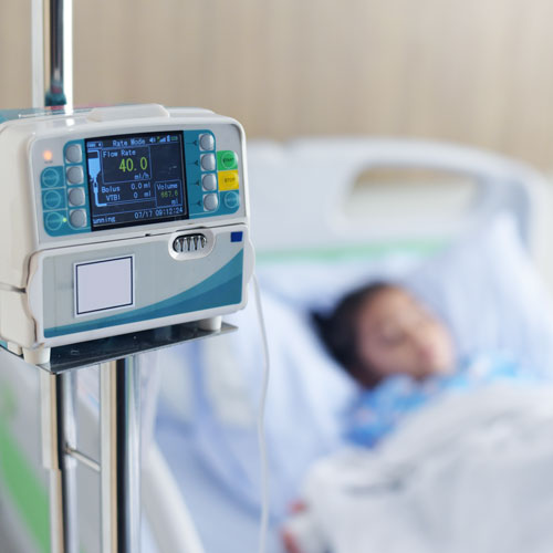 A young patient lies in bed next to an intravenous infusion pump.