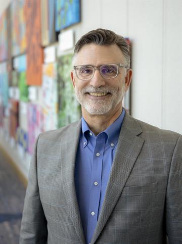 A smiling Rob Jensen faces the camera while standing in a long hallway.