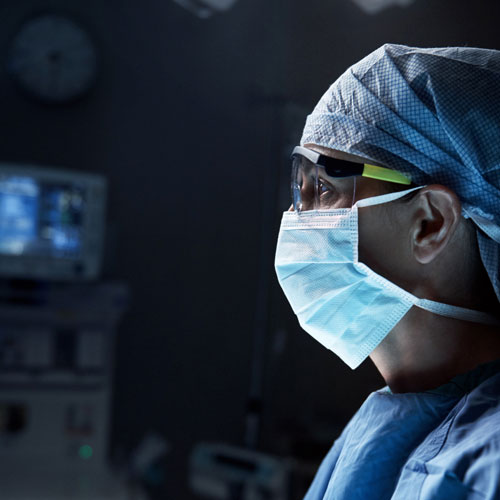 A surgeon wearing a mask with medical devices in the background.